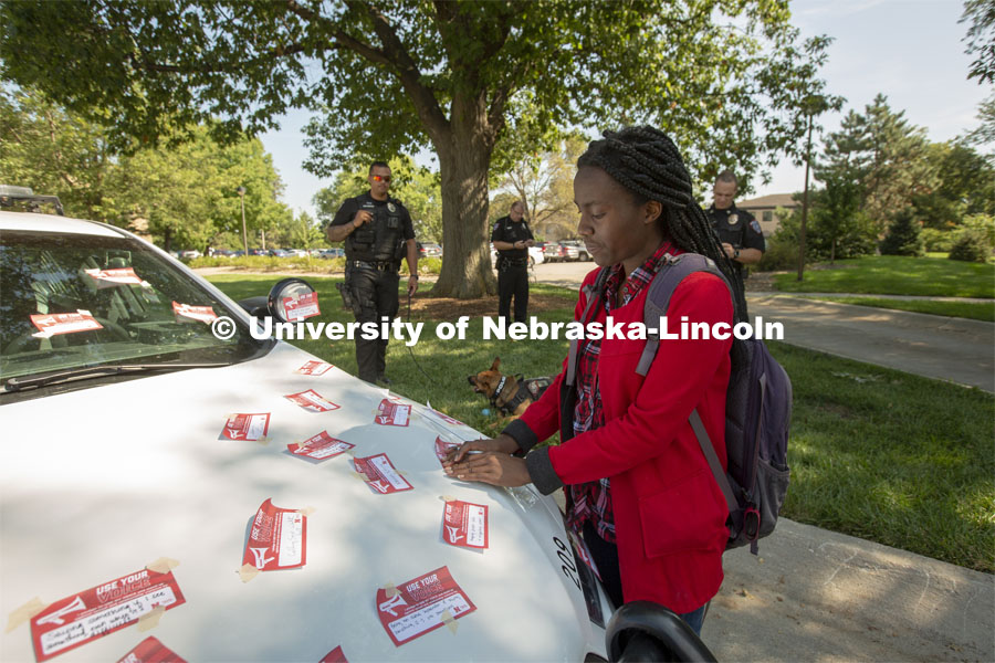 Elizabeth Uwase, a junior integrated science major from Rwanda, affixes her "Use Your Voice" pledge to a police car during the September 10 Cover the Cruiser event on East Campus. More than 75 students, faculty and staff made a pledge to stand up to sexual violence in the first day of the initiative. September 10, 2019.  Photo by Troy Fedderson / University Communication.